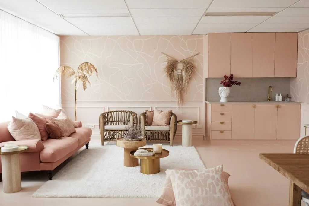 A dusky pink living area in an open plan office featuring decorative skirting and wainscoting. A white rug sits on a dusky pink carpet surrounded by a lounge and stylish nested coffee tables.