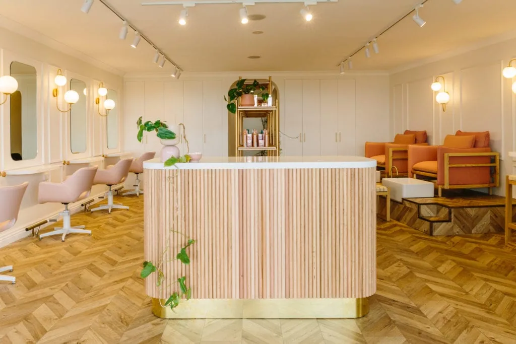 A mid-century modern hair salon featuring light parquetry flooring, natural wooden materials, and comfortable lounge chairs.