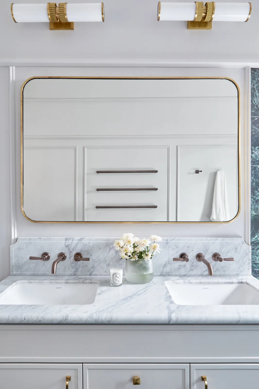 Dual-sink vanity with marble countertops, brass fixtures, and a gold-framed mirror—mouldings elevate the bathroom’s classic luxury aesthetic.