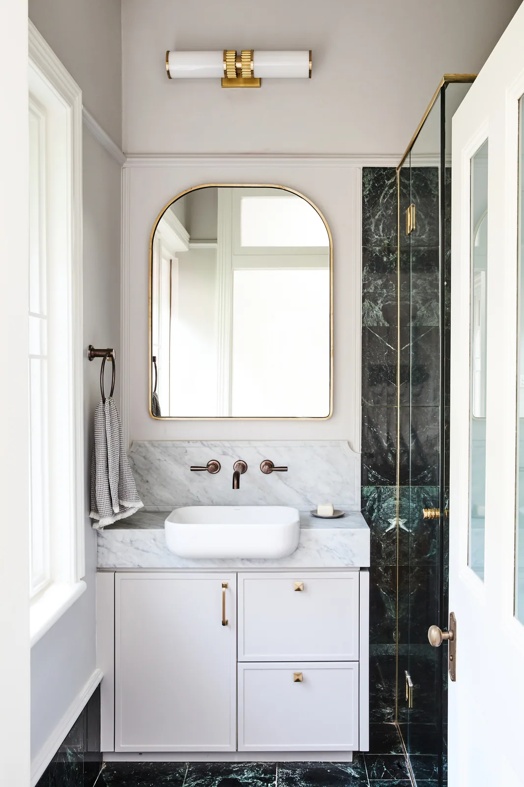 Bathroom featuring dark marble shower tiles and white vanity—clean moulding lines balance bold material contrasts for a timeless look.
