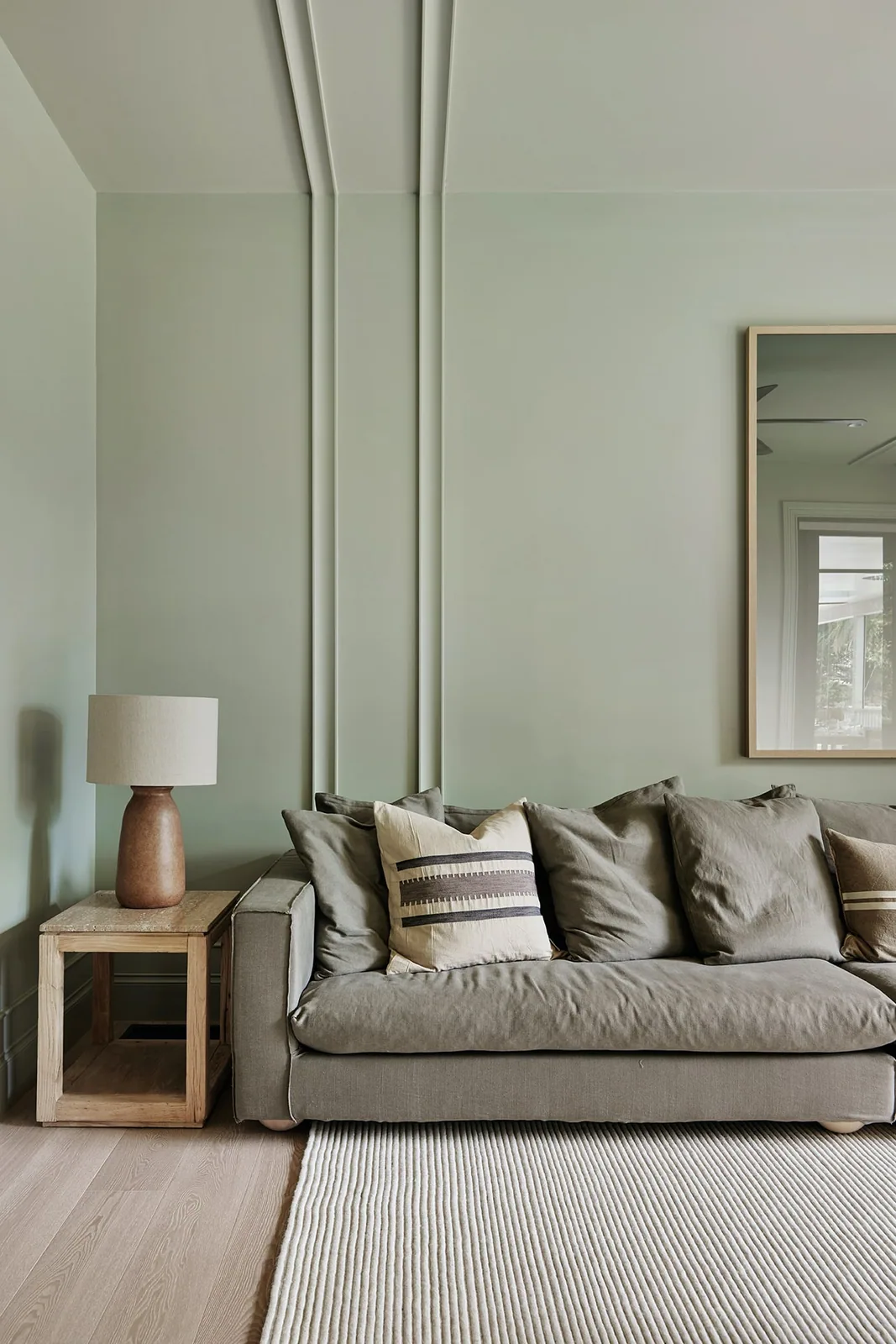Contemporary living room with soft green wall and ceiling panelling, featuring slim vertical mouldings behind a neutral sofa.