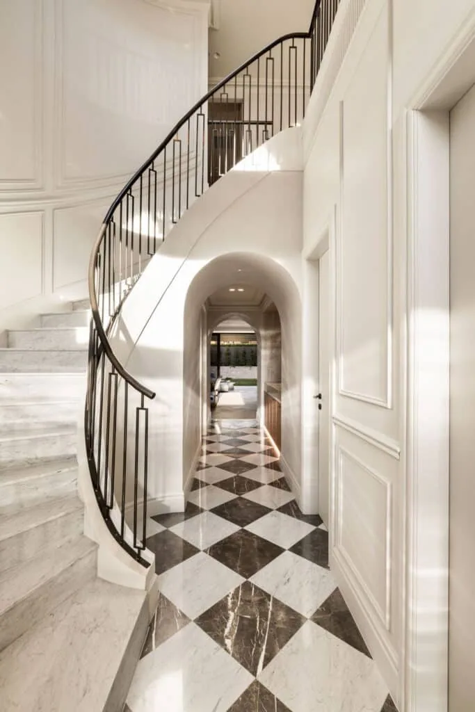 Grand staircase with curved detailing, elevated by decorative wall panelling, refined mouldings, and an arched passage that creates a sculptural architectural statement.