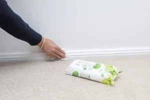 A woman's hand using a disinfectant wipe to clean wall skirting