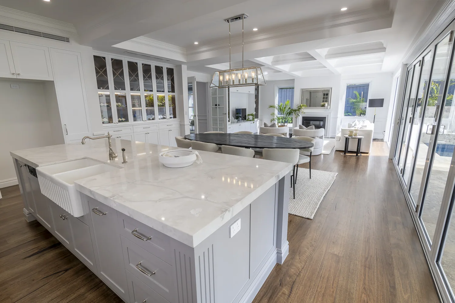 Open-plan kitchen and living area featuring decorative timber mouldings, detailed coffered ceiling panels, classic cornice, and panelled cabinetry with skirting continuity