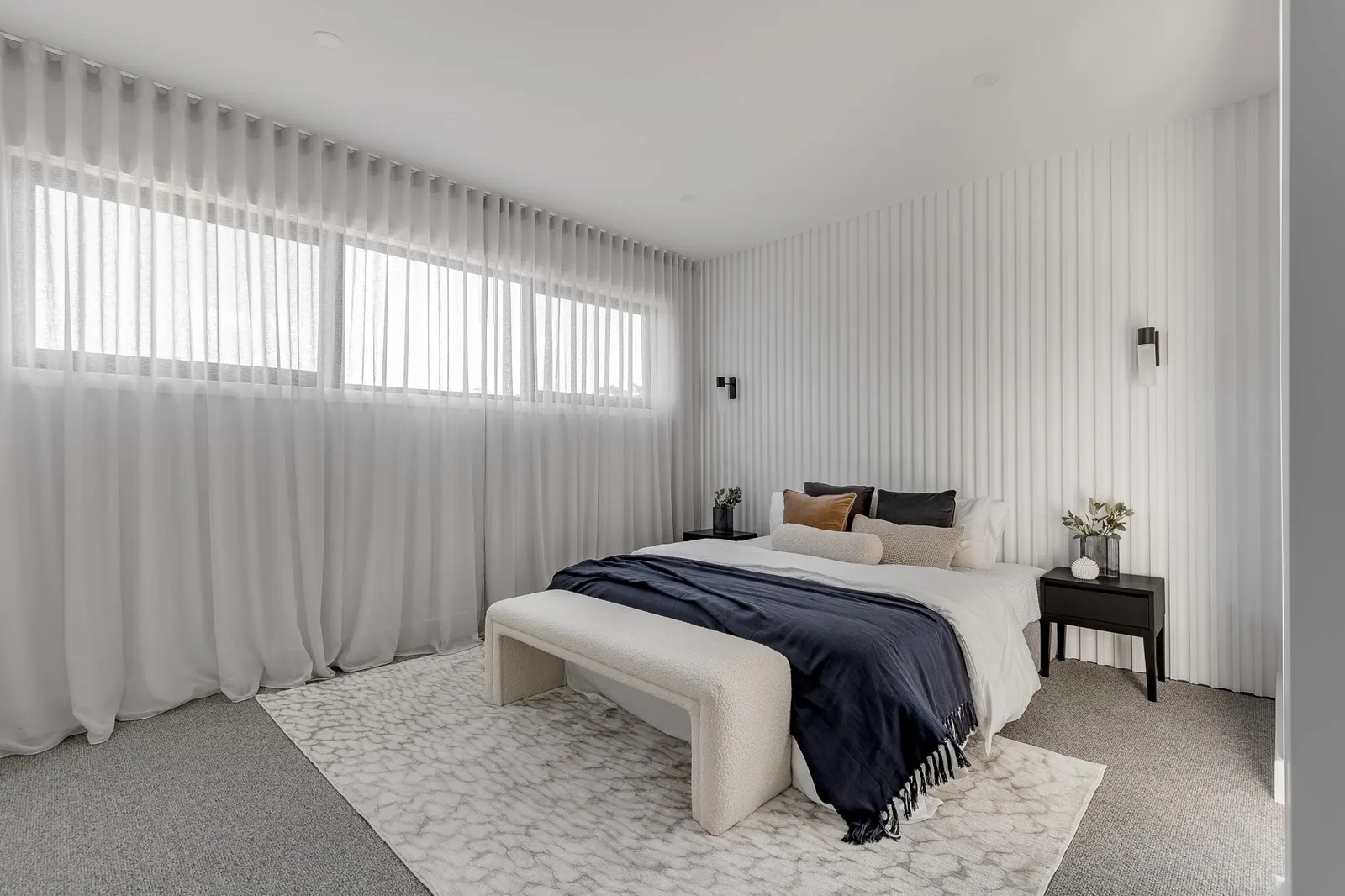 Bedroom with full-height fluted wall panelling, adding soft texture behind a neutral bed setting.