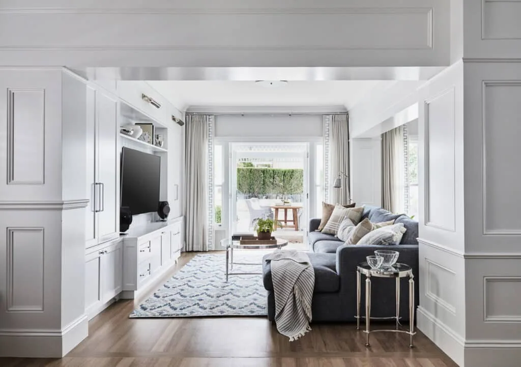 Light-filled living room framed with decorative wall panelling and detailed mouldings, creating architectural definition around a relaxed, coastal-inspired interior.