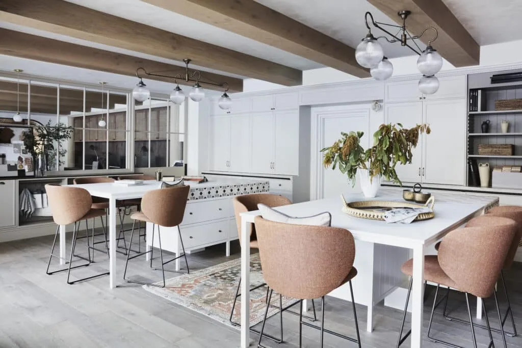 An open plan office space featuring breakout bar tables and dusty pink upholstered chairs. Light timber floorboards and white walls bring brightness to the space.