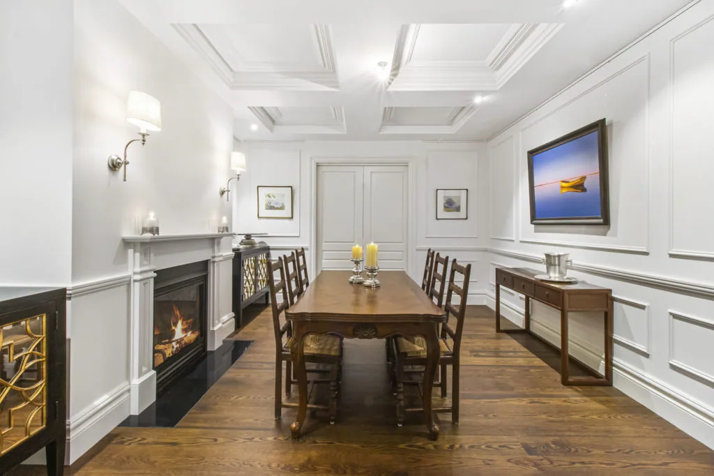 Classic dining room elevated with decorative wall panelling, coffered ceiling mouldings, and a detailed fireplace surround.