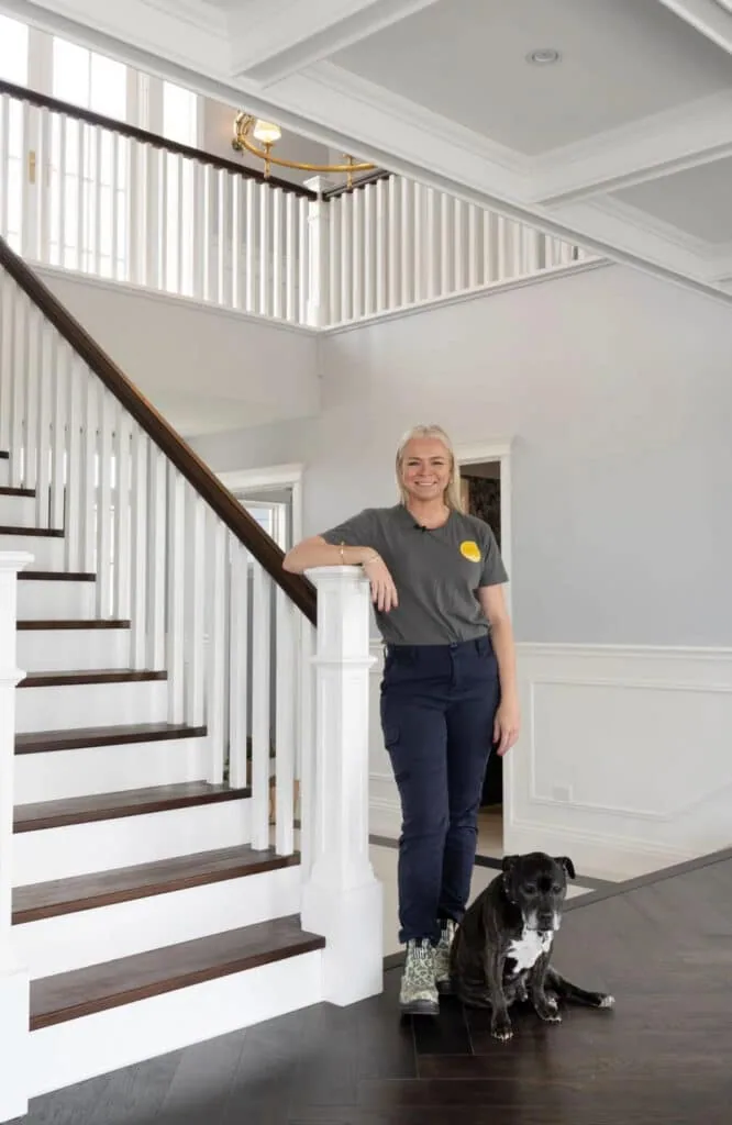 Rachael Turner of Front Porch Properties leaning against a banister in a modern entryway with a black and white dog by her feet.