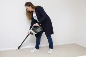 A woman using a vacuum cleaner to dust skirting boards