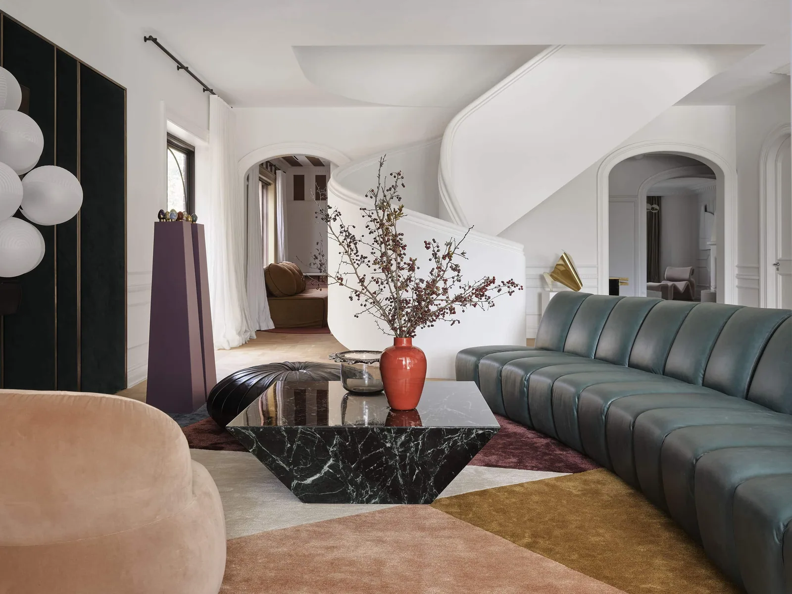 Living room at Matchpoint House Strathfield by Duet, featuring a teal leather modular sofa, black marble geometric coffee table, colourful patchwork rug and a sculptural curved white staircase framed by arched openings